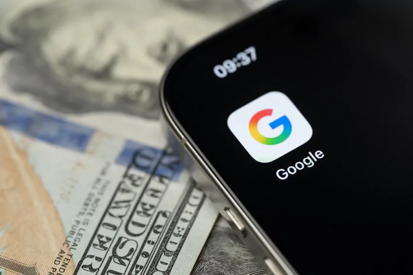 Na stole leży smartfon. Na jego ekranie wyświetlona jest aktualna godzina. Widnieje na nim też ikonka konta Google.